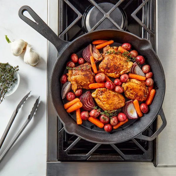 Cast iron skillet on a stove filled with roasted chicken and vegetables